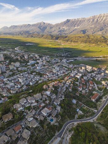 Aerial view of the historic city of Gjirokaster with traditional stone houses winding streets and a lush green valley set against a mountain range in Gjirokaster Gjirokaster County Albania. Aerial view of the historic city of Gjirokaster with traditional stone houses winding streets and a lush green valley set against a mountain range in Gjirokaster Gjirokaster County Albania.