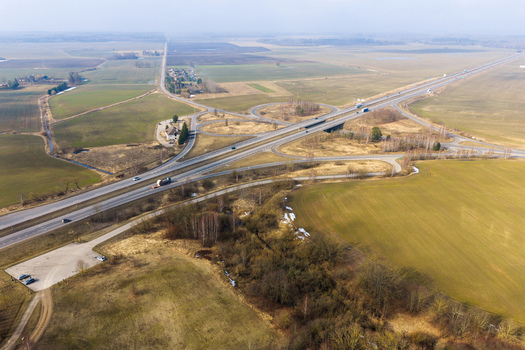 Aerial view of a highway interchange with cloverleaf ramps and surrounding agricultural fields under a clear sky Lithuania.
