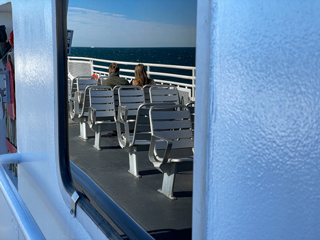 View of the passenger deck on a ferry with empty metal seats and a couple looking out at the blue ocean near Martha s Vineyard Edgartown Massachusetts United States.