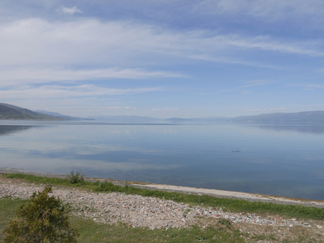View of the calm waters of Lake Ohrid with distant mountains under a clear blue sky in Pogradec Korce County Albania. View of the calm waters of Lake Ohrid with distant mountains under a clear blue sky in Pogradec Korce County Albania.