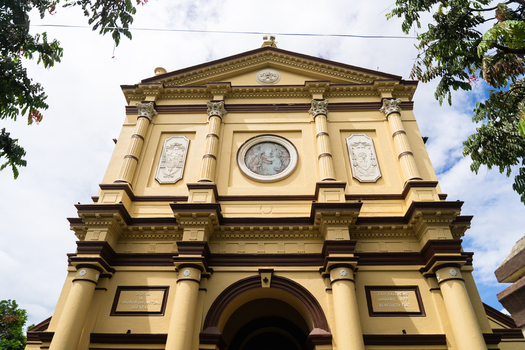 View of the historic St. Anthony s Cathedral featuring a yellow facade with classical columns and religious artwork under a cloudy sky in Kandy Central Province Sri Lanka. View of the historic St. Anthony s Cathedral featuring a yellow facade with classical columns and religious artwork under a cloudy sky in Kandy Central Province Sri Lanka.