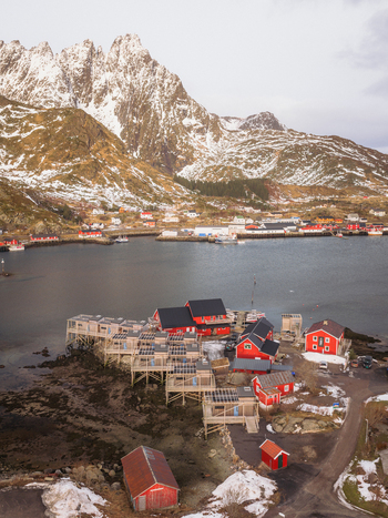 Aerial view of red cabins dotting the rugged coastline nestled against the snow dusted mountains and calm waters a picturesque scene Ballstad Nordland Norway. Aerial view of red cabins dotting the rugged coastline nestled against the snow dusted mountains and calm waters a picturesque scene Ballstad Nordland Norway.
