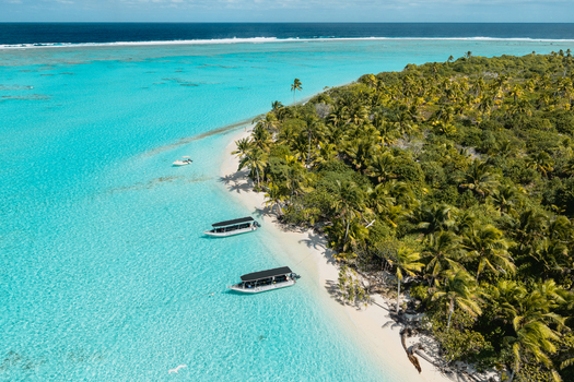 Aerial view of Aitutaki island with lush palm trees white sand beach and boats anchored in the clear turquoise lagoon of the Cook Islands. Aerial view of Aitutaki island with lush palm trees white sand beach and boats anchored in the clear turquoise lagoon of the Cook Islands.