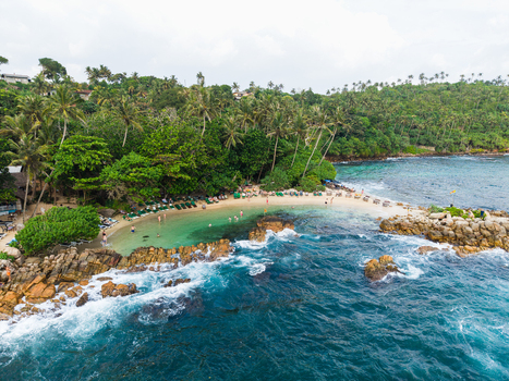 Aerial view of Secret Beach Mirissa with turquoise waters rocky shores and lush palm trees with people enjoying the tropical coastline in Mirissa Southern Province Sri Lanka. Aerial view of Secret Beach Mirissa with turquoise waters rocky shores and lush palm trees with people enjoying the tropical coastline in Mirissa Southern Province Sri Lanka.