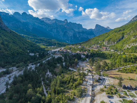 Aerial view of Theth village nestled in the Albanian Alps with lush green forests rocky riverbeds and traditional houses under a clear blue sky in Theth Shkoder County Albania. Aerial view of Theth village nestled in the Albanian Alps with lush green forests rocky riverbeds and traditional houses under a clear blue sky in Theth Shkoder County Albania.