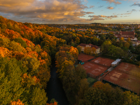 Aerial view of golden autumn foliage embracing the Neris River juxtaposed against red clay tennis courts under a dramatic sky Vilnius Lithuania. Aerial view of golden autumn foliage embracing the Neris River juxtaposed against red clay tennis courts under a dramatic sky Vilnius Lithuania.