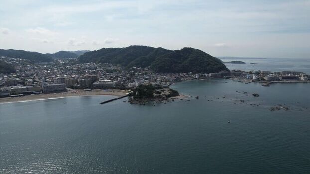Aerial view of Morito Coast featuring the sandy beach coastal town buildings and lush green hills along the shoreline in Hayama Kanagawa Japan.