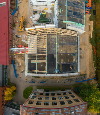 Aerial view of a construction site featuring wooden roof trusses building materials and heavy machinery adjacent to a multi story building in Latvia. Aerial view of a construction site featuring wooden roof trusses building materials and heavy machinery adjacent to a multi story building in Latvia.