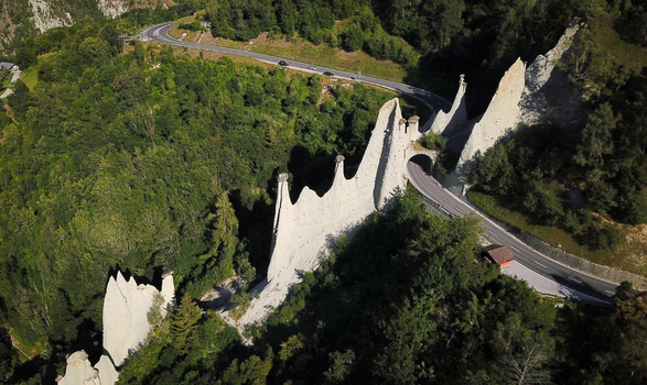 Aerial view of Pyramides d Euseigne earth pyramids with a road tunnel passing through the rock formations surrounded by dense green forest Heremence Valais Switzerland. Aerial view of Pyramides d Euseigne earth pyramids with a road tunnel passing through the rock formations surrounded by dense green forest Heremence Valais Switzerland.