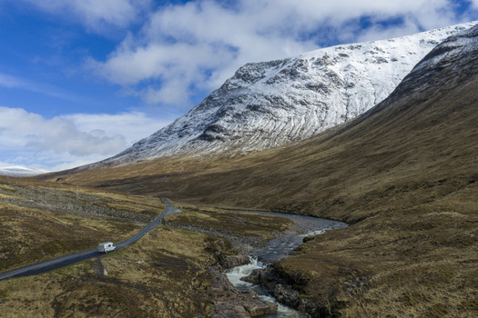 Aerial view of Glen Etive Waterfall View Point with a winding road a campervan and snow capped mountains in Ballachulish Scotland United Kingdom.