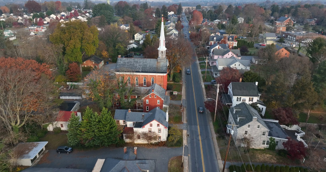 Aerial view of a historic church with a white steeple surrounded by residential houses autumn trees and a road in Millersville Pennsylvania United States. Aerial view of a historic church with a white steeple surrounded by residential houses autumn trees and a road in Millersville Pennsylvania United States.