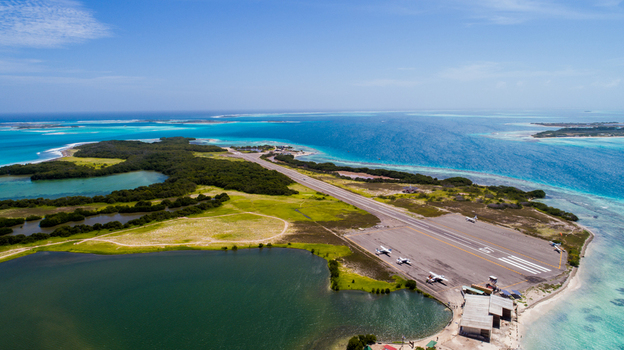 Aerial view of the Los Roques archipelago airport runway surrounded by turquoise Caribbean waters and lush green vegetation in Los Roques Dependencias Federale Venezuela. Aerial view of the Los Roques archipelago airport runway surrounded by turquoise Caribbean waters and lush green vegetation in Los Roques Dependencias Federale Venezuela.