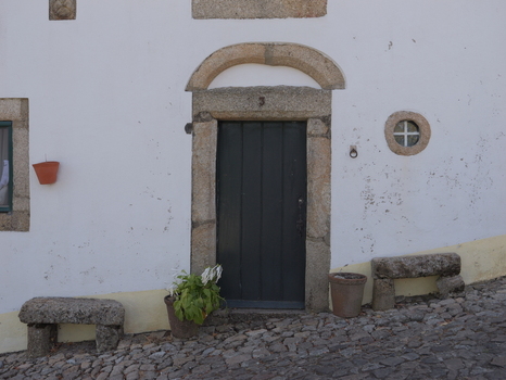View of a traditional stone doorway with a dark wooden door a small circular window and stone benches on a cobblestone street in Marvao Portalegre District Portugal. View of a traditional stone doorway with a dark wooden door a small circular window and stone benches on a cobblestone street in Marvao Portalegre District Portugal.