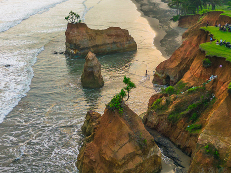 Aerial view of dramatic coastal cliffs with unique rock formations rising from the sea lush green grass on the cliff edge and gentle waves in Bali Bali Indonesia. Aerial view of dramatic coastal cliffs with unique rock formations rising from the sea lush green grass on the cliff edge and gentle waves in Bali Bali Indonesia.