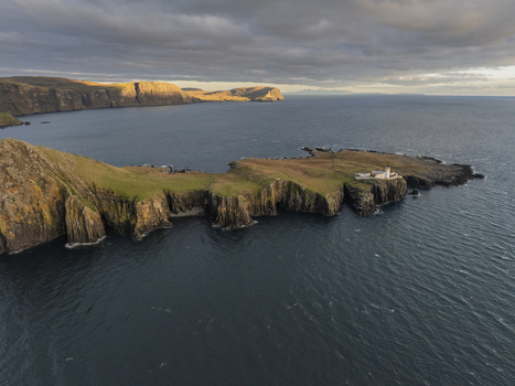 Aerial view of Neist Point Lighthouse situated on a dramatic rocky peninsula with steep cliffs lush green grass and deep blue sea under a cloudy sky Scotland United Kingdom. Aerial view of Neist Point Lighthouse situated on a dramatic rocky peninsula with steep cliffs lush green grass and deep blue sea under a cloudy sky Scotland United Kingdom.