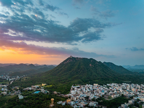 Aerial view of the cityscape nestled among the lush green Aravalli hills during sunset in Udaipur Rajasthan India.