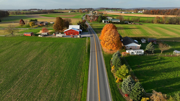 Aerial view of a rural road cutting through farmland with a red barn autumn foliage and residential properties in Rapho Pennsylvania United States. Aerial view of a rural road cutting through farmland with a red barn autumn foliage and residential properties in Rapho Pennsylvania United States.