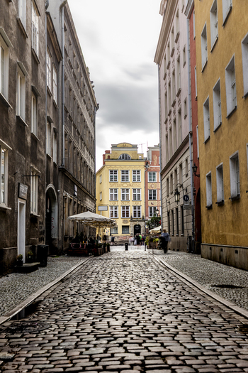 View of a narrow cobblestone street in the historic old town flanked by colorful buildings with cafe seating and pedestrians in Gdansk Pomeranian Voivodeshi Poland. View of a narrow cobblestone street in the historic old town flanked by colorful buildings with cafe seating and pedestrians in Gdansk Pomeranian Voivodeshi Poland.