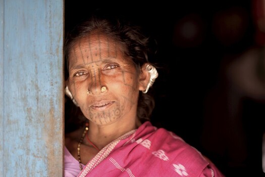 Odisha India 26 March 2026 View of an indigenous woman with traditional tattoos and a nose ring framed by a weathered blue doorway her face a canvas of stories etched in time. Odisha India 26 March 2026 View of an indigenous woman with traditional tattoos and a nose ring framed by a weathered blue doorway her face a canvas of stories etched in time.