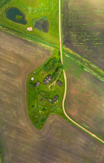 Aerial view of a rural farmstead nestled among agricultural fields with a dirt road and small ponds in Latvia. Aerial view of a rural farmstead nestled among agricultural fields with a dirt road and small ponds in Latvia.
