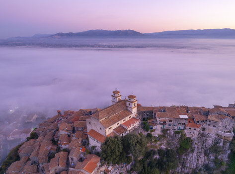 Aerial view of the historic town of Artena with its dense cluster of terracotta roofed buildings and church towers rising above a thick layer of morning fog in Artena Lazio Italy.