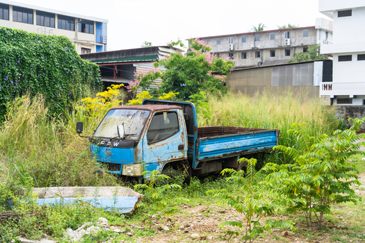 View of an abandoned blue truck parked in a field of overgrown grass and weeds with buildings in the background Galle Southern Province Sri Lanka. View of an abandoned blue truck parked in a field of overgrown grass and weeds with buildings in the background Galle Southern Province Sri Lanka.