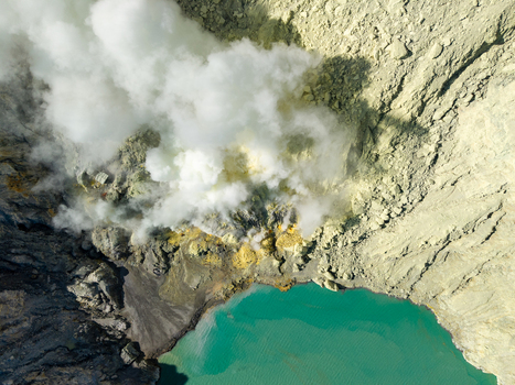Aerial view of Mount Ijen sulfur mining operations with thick volcanic smoke rising from the crater near the turquoise acidic lake in Ijen East Java Indonesia.