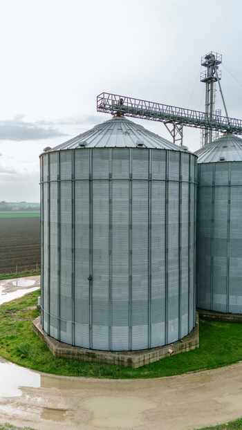Aerial view of towering silver grain silos rise against the muted green fields their metallic surfaces reflecting the overcast sky Sremska Mitrovica Vojvodina Serbia. Aerial view of towering silver grain silos rise against the muted green fields their metallic surfaces reflecting the overcast sky Sremska Mitrovica Vojvodina Serbia.