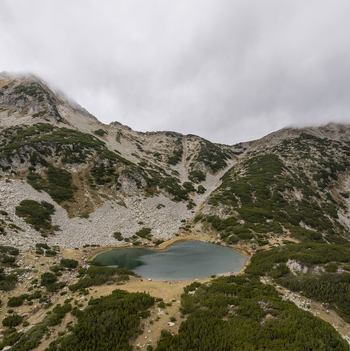 Aerial view of Muratovo Lake nestled within the rocky peaks of Pirin National Park featuring alpine vegetation and a cloudy sky in Blagoevgrad Province Bulgaria. Aerial view of Muratovo Lake nestled within the rocky peaks of Pirin National Park featuring alpine vegetation and a cloudy sky in Blagoevgrad Province Bulgaria.