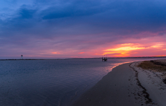 View of the sandy shoreline and Edgartown Harbor Light under a vibrant purple and orange sunset sky on Martha s Vineyard Edgartown Massachusetts United States.