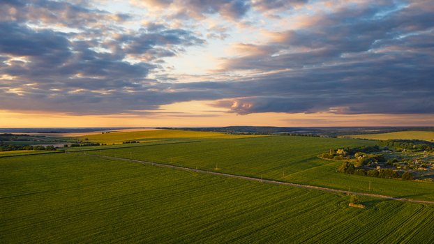 Aerial view of a sprawling green field meeting a horizon of golden sunlight under a vast dramatic sky Skarzhynka Cherkasy Oblast Ukraine. Aerial view of a sprawling green field meeting a horizon of golden sunlight under a vast dramatic sky Skarzhynka Cherkasy Oblast Ukraine.