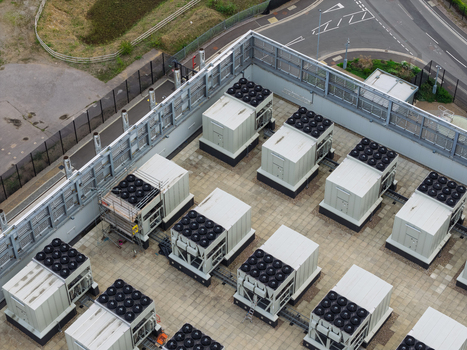 Aerial view of a data center rooftop featuring multiple industrial cooling units and HVAC systems on a paved surface in the United Kingdom.