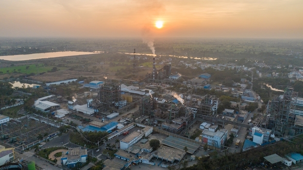 Aerial view of an industrial plant with complex machinery and smoking chimneys surrounded by fields under a warm sunset sky in Nagda Madhya Pradesh India. Aerial view of an industrial plant with complex machinery and smoking chimneys surrounded by fields under a warm sunset sky in Nagda Madhya Pradesh India.