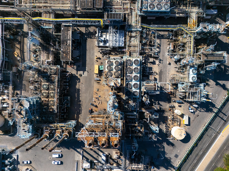 Aerial view of an industrial oil refinery complex featuring intricate piping networks cooling fans storage tanks and industrial infrastructure in Carson California United States.