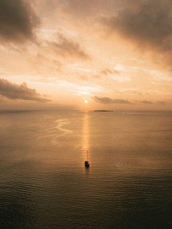 Aerial view of a lone boat sailing on the tranquil golden sea under a warm cloudy sky Pine Island L &Icirc;le des Pins New Caledonia.