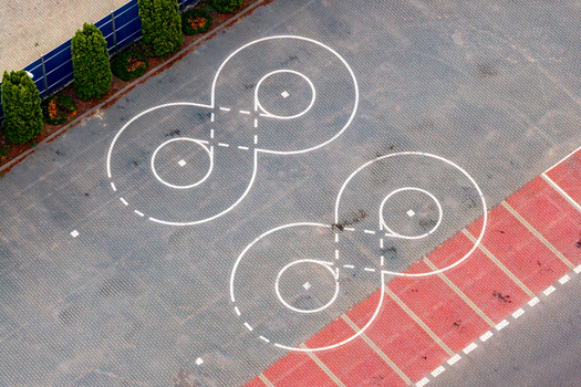 Aerial view of two white infinity shaped markings painted on a paved parking lot with green bushes and a blue fence in Warsaw Masovian Voivodeship Poland. Aerial view of two white infinity shaped markings painted on a paved parking lot with green bushes and a blue fence in Warsaw Masovian Voivodeship Poland.