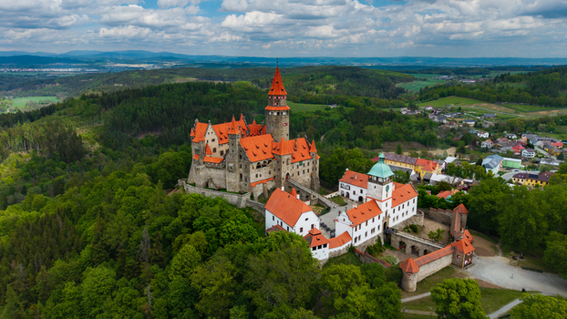 Aerial view of Bouzov Castle with its iconic red roofs and tall stone tower surrounded by lush green forests under a cloudy sky in Bouzov Olomoucky kraj Czechia. Aerial view of Bouzov Castle with its iconic red roofs and tall stone tower surrounded by lush green forests under a cloudy sky in Bouzov Olomoucky kraj Czechia.