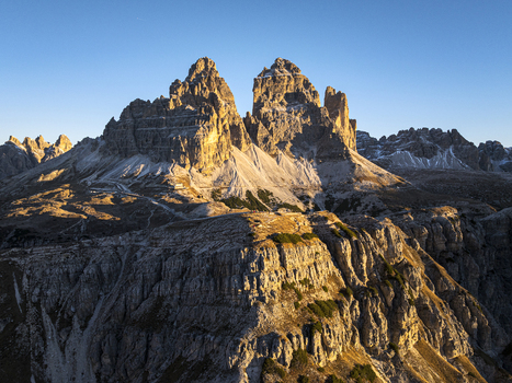 Aerial view of the iconic Tre Cime di Lavaredo peaks basks in the warm glow of the setting sun Misurina Veneto Italy. Aerial view of the iconic Tre Cime di Lavaredo peaks basks in the warm glow of the setting sun Misurina Veneto Italy.