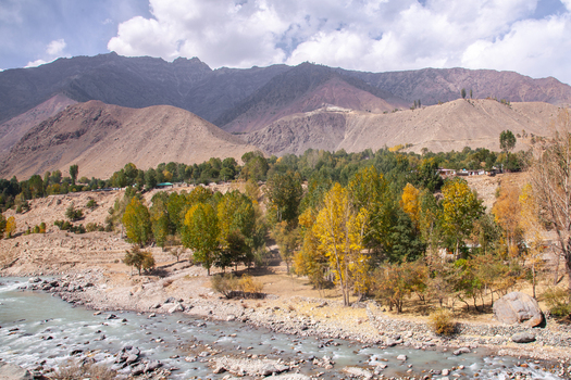 View of the Astore Valley with a flowing river autumn foliage on trees and rugged mountains under a cloudy sky in Astore Gilgit Pakistan. View of the Astore Valley with a flowing river autumn foliage on trees and rugged mountains under a cloudy sky in Astore Gilgit Pakistan.
