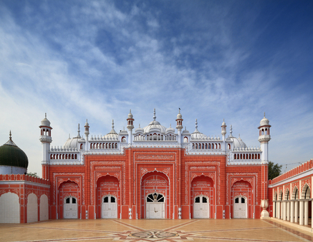 View of the ornate red and white facade of the historic Shahi Mosque with intricate carvings domes and minarets under a clear blue sky in Chiniot Punjab Pakistan.