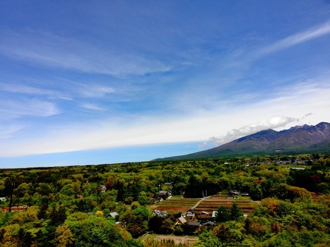 Aerial view of the lush green foothills of the Yatsugatake Mountains with small houses and agricultural fields under a bright blue sky in Chino Nagano Japan. Aerial view of the lush green foothills of the Yatsugatake Mountains with small houses and agricultural fields under a bright blue sky in Chino Nagano Japan.