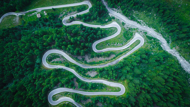 Aerial view of a winding serpentine mountain road snaking through a dense green pine forest in the Swiss Alps Heremence Valais Switzerland. Aerial view of a winding serpentine mountain road snaking through a dense green pine forest in the Swiss Alps Heremence Valais Switzerland.