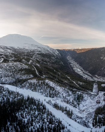 Aerial view of the snow covered Gaustatoppen mountain and valley near Rjukan featuring ski slopes pine forests and a winding road under a soft winter sky in Rjukan Telemark Norway. Aerial view of the snow covered Gaustatoppen mountain and valley near Rjukan featuring ski slopes pine forests and a winding road under a soft winter sky in Rjukan Telemark Norway.