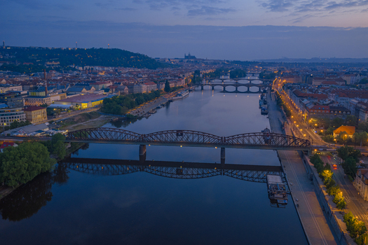 Aerial view of the Vltava river at twilight with the historic Vysehrad railway bridge reflecting in the calm water surrounded by the illuminated cityscape of Prague Prague Czechia.