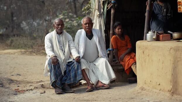 View of elderly men and a girl sitting outside a hut in India.