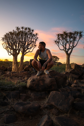 Quiver Tree Forest Namibia 06 March 2026 View of a man perched on a rock amidst the iconic quiver trees their silhouettes stark against the warm hues of the setting sun. Quiver Tree Forest Namibia 06 March 2026 View of a man perched on a rock amidst the iconic quiver trees their silhouettes stark against the warm hues of the setting sun.