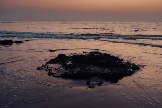 View of the serene beach with a dark rock formation contrasting the soft pastel sky and gentle waves reflecting the tranquil dawn Chiplun Maharashtra India. View of the serene beach with a dark rock formation contrasting the soft pastel sky and gentle waves reflecting the tranquil dawn Chiplun Maharashtra India.