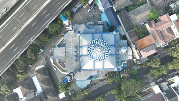 Aerial view of a mosque with a prominent blue and white patterned dome and minarets situated near a highway and residential area in Bekasi Barat West Java Indonesia. Aerial view of a mosque with a prominent blue and white patterned dome and minarets situated near a highway and residential area in Bekasi Barat West Java Indonesia.