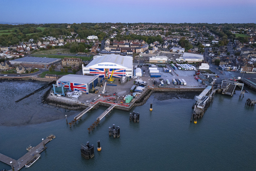 Aerial view of the Wight Shipyard Co facilities featuring large industrial buildings with Union Jack motifs piers and boats along the waterfront in Cowes England United Kingdom.