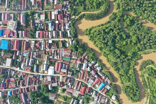 Aerial view of Pulau Maginti showing dense residential rooftops adjacent to a winding river and lush tropical vegetation in Maginti South East Sulawesi Indonesia.